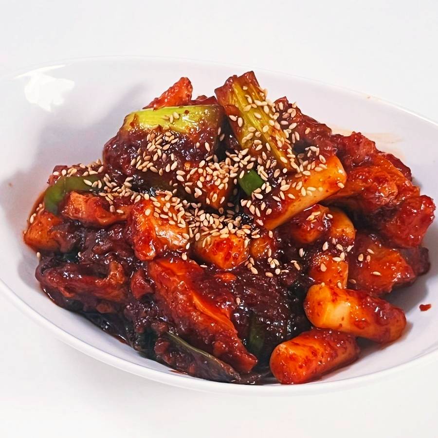 plated Korean spicy chicken with rice cakes sesame seeds and green onions